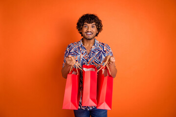 Photo portrait of nice young man hold peek shopping bags wear trendy colorful outfit isolated on orange color background