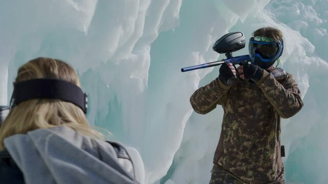 Female paintballer shooting masked man in ice fortress - medium shot