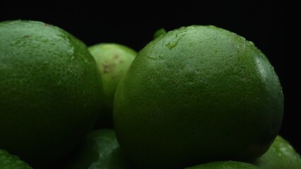 Slices of lime are meticulously arranged in a pile, set against a black background. Each lime slice is captured in stunning detail, its vibrant green hue and enticing texture. Close up. Comestible.