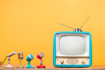 Retro TV and old microphones front yellow wall background. Vintage style filtered photo