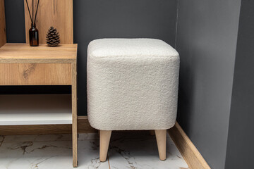 Square pouf with wooden legs. White pouf in hallway. Upholstery faux fur