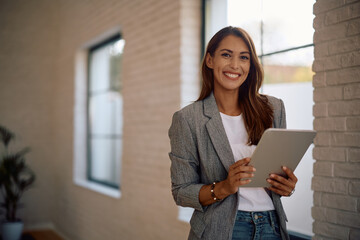 Happy businesswoman using digital tablet in office and looking at camera.
