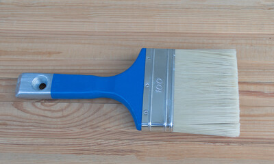 A blue and white paintbrush with bristles on the wooden table is used for painting walls