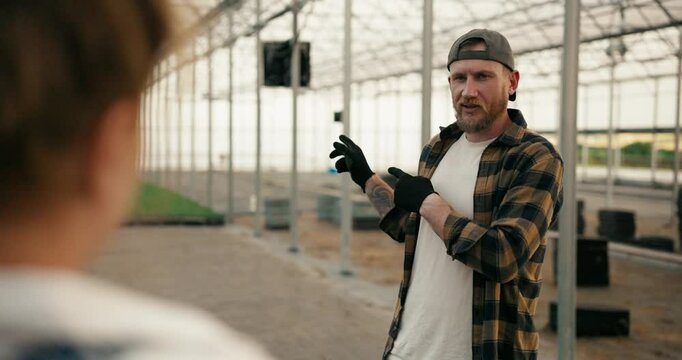 Over the shoulder a confident guy in a cap with a beard in a plaid shirt communicates with a girl with red hair while designing a greenhouse and working on a farm