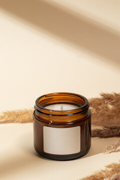Amber glass candle with pampas grass on beige background