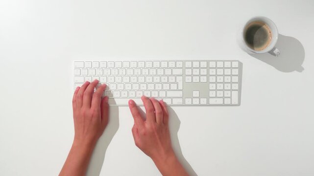Overhead shot of hands typing on computer keyboard, drinking coffee