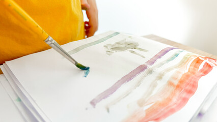 The kid paints with a brush with watercolors, a rainbow and a bunny. Early development of children through creativity. Children's creativity using paints.