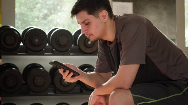 Close-Up of a Man Checking His Phone During Gym Training. Focused Moment with Technology in a Workout Setting.