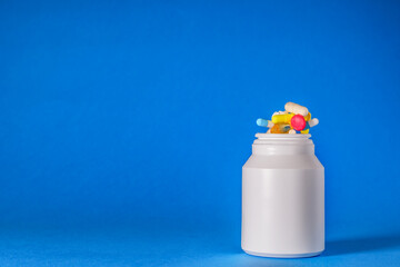 Pill, drug bottle with tablets coming out the top onto a isolated blue background. Drug cocktail, Medical, pharmaceutical concept image.  