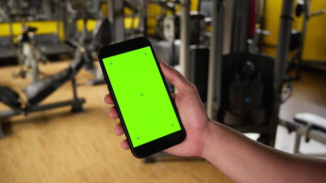 Green Screen Smartphone in Gym for Fitness Apps and Health Ads. Smartphone with green screen held in a gym, perfect for fitness and health app advertisements or promotional videos.