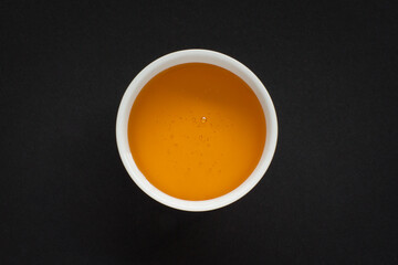 Close up of honey in a small white bowl with a honey dipper stick on black background