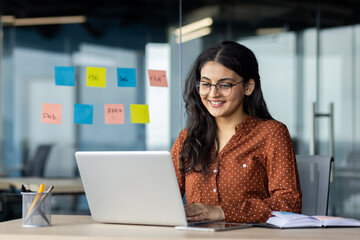 Happy and smiling hispanic businesswoman typing on laptop, office worker with curly hair and...