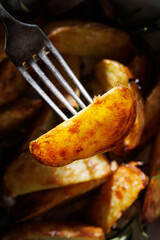 Close up of roasted potato wedge  seasoned with aromatic herbs and garlic, focus on potato wedge inside 