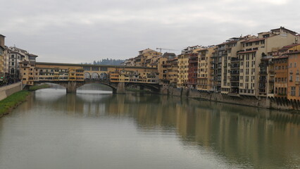 Naklejka premium Florence, Italy - decembre 27 2024: Sunny Tuscany with iconic Ponte Vecchio, Florence skyline historic architecture, Arno River reflections. A colorful blend of Renaissance culture, medieval landmarks