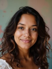 Naklejka premium A close-up portrait of a young woman with curly hair, smiling warmly and looking directly at the camera, against a softly blurred pastel background.
