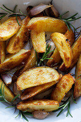 Baked potato wedges seasoned with rosemary and garlic on a white background, close-up