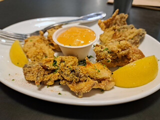 Restaurant food - a white plate with fried breaded oysters, a cup of sauce, and lemon wedges
