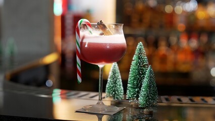 Focusing mixed punch cocktail christmas theme garnished with candy cane and cinnamon serving on luxury counter bar beside by green neon snow of Christmas tree special festive advertisement. Vinosity.