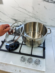 In a wellequipped kitchen for culinary creativity, a person holds a pot lid over a stove, ready to check or add ingredients, showcasing the art of cooking and food preparation