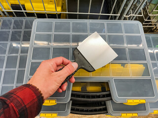 A hand is firmly grasping a putty knife positioned just above a storage container that features...