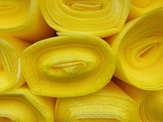 A collection of bright yellow rolls of fabric are carefully stacked on top of one another, creating a visually interesting display and showcasing their vibrant color and texture