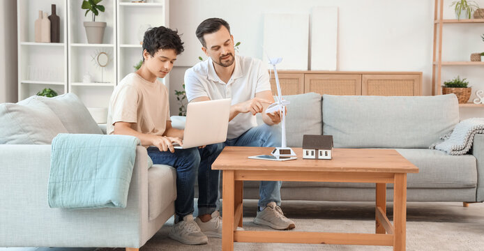 Teenage boy and his father with wind turbine model using laptop on sofa at home