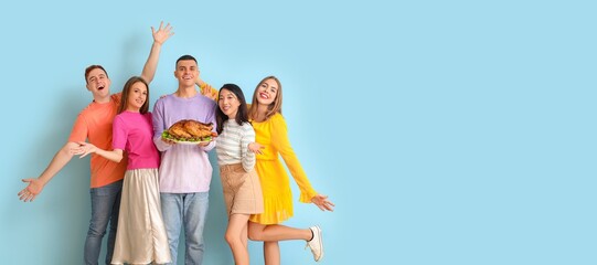 Happy friends holding tasty baked turkey on light blue background with space for text. Thanksgiving Day celebration