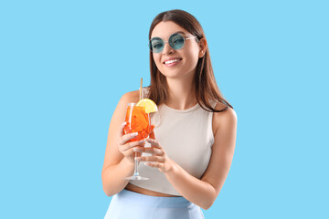 Beautiful young woman with glass of tasty aperol spritz cocktail on blue background