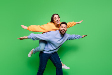 Photo of glad funny cheerful couple wear trendy clothes have fun piggy back isolated on green color background