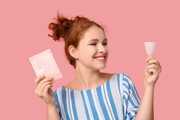 Beautiful young woman with menstrual cup and pad on pink background