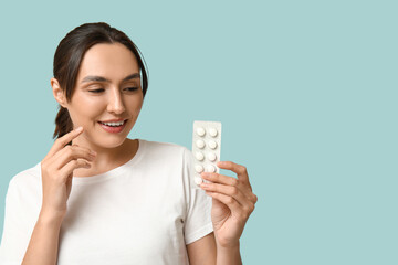 Pretty young woman with pills on blue background