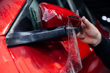 The master applies vinyl film to the side view mirror of a car. 