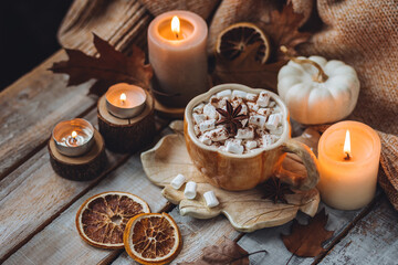 Spicy sweet fall hot drink: delicious pumpkin latte with cinnamon, marshmallow with salted caramel. Served in handmade artisan mug in shape of pumpkins, cozy home decor with candles, dry autumn leaves