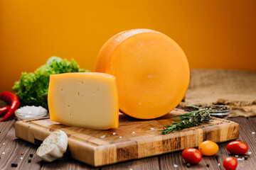Golden cheese wheel and slice on wooden board, ideal for food photography and culinary presentations