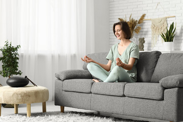 Young woman meditating while sitting on sofa at home