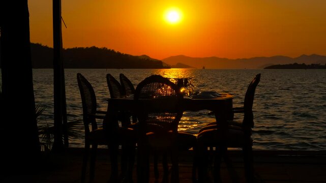Romantic sunset dinner on the beach. Silhouette of a served empty table at sunset