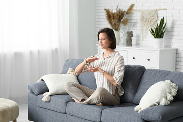 Obraz premium Young woman meditating while sitting on sofa at home