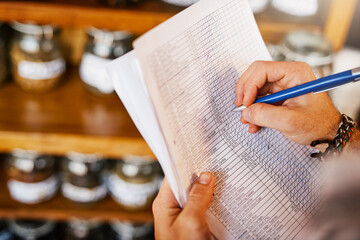 Hands, shop owner and writing with paperwork in cafe with review for inventory, stock and ingredients. Person, documents and checklist with notes by shelf for coffee, tea and stats at restaurant