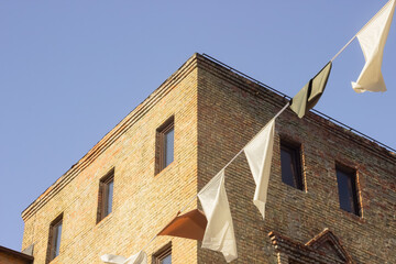 A vibrant summer scene featuring the corner of an industrial brick building under a bright blue sky. Sunlight illuminates the walls, while colorful festival flags hang in the foreground.