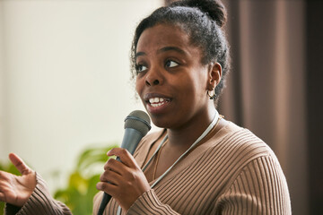 Young African American woman giving speech while holding microphone and gesturing with hand Demonstrating expression of engagement and confidence