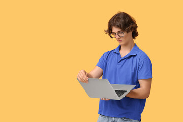 Male programmer in eyeglasses working with laptop on orange background