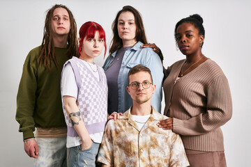 Portrait of group of five young adults of diverse ethnic backgrounds standing together against...