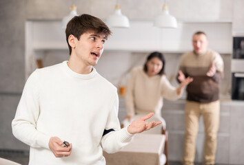 Obraz premium Adult man and young woman during family quarrel with young guy in kitchen