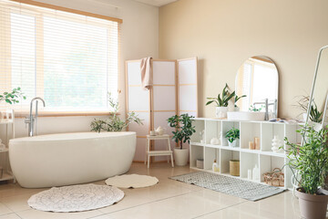 Interior of bathroom with bathtub, shelving unit, houseplants and folding screen