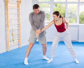 Obraz premium Dynamic young female attendee of self-defense classes and middle-aged trainer performing arm-lock technique in sports hall