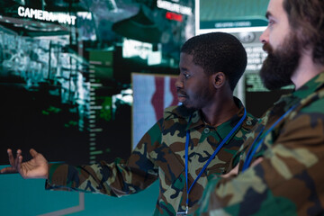Fototapeta premium Diverse special operation engineers examine real time information on a big screen, collecting intelligence to aid troopers during military operations. IT professionals work on reconnaissance.