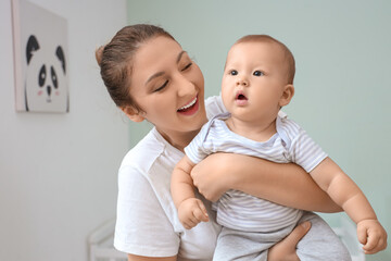 Beautiful young happy mother with cute little baby in children's room at home