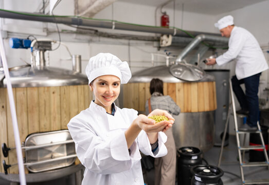 Portrait of positive woman brewmaster holding bunch of hops pellets in beer factory. - Powered by Adobe