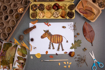 a craft project on a flat surface. At the center is a zebra creatively decorated with natural elements like leaves and twigs, various crafting materials