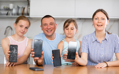 Happy family of four showing the screens of their phones